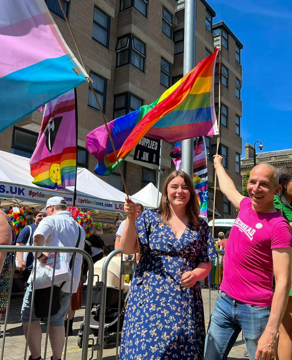 Sophie holding a trans flag at a pride celebration